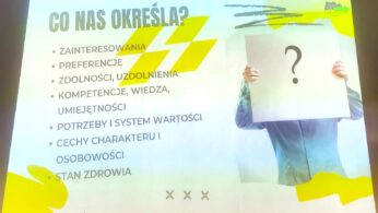 Slajd prezentacji w języku polskim zatytułowany CO NAS OKREŚLA? wymienia cechy, które nas definiują, takie jak zainteresowania, preferencje, zdolności, umiejętności, wiedza, wartości, osobowość i zdrowie. Po prawej stronie osoba trzyma papier z dużym znakiem zapytania zakrywającym jej twarz.