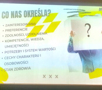 Slajd prezentacji w języku polskim zatytułowany CO NAS OKREŚLA? wymienia cechy, które nas definiują, takie jak zainteresowania, preferencje, zdolności, umiejętności, wiedza, wartości, osobowość i zdrowie. Po prawej stronie osoba trzyma papier z dużym znakiem zapytania zakrywającym jej twarz.