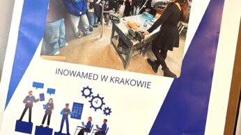 Duży plakat na sztaludze przedstawia zdjęcie studentów słuchających kobiety w warunkach laboratoryjnych. Polski tekst brzmi Wizyty studyjne - Zawodoznawcze i Inowamed w Krakowie. U dołu widnieją logotypy UE, Polski i władz lokalnych.