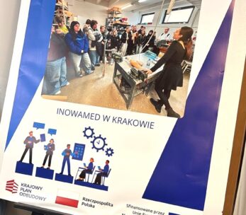 Duży plakat na sztaludze przedstawia zdjęcie studentów słuchających kobiety w warunkach laboratoryjnych. Polski tekst brzmi Wizyty studyjne - Zawodoznawcze i Inowamed w Krakowie. U dołu widnieją logotypy UE, Polski i władz lokalnych.