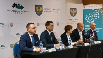 Pięć osób w strojach biznesowych siedzi przy stole z mikrofonami i butelkami wody, uczestnicząc w oficjalnej konferencji prasowej. Za nimi znajdują się banery i logotypy Wojewódzkiego Urzędu Pracy i samorządu województwa opolskiego.