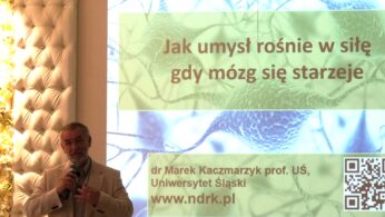 Mężczyzna w jasnym garniturze mówi do mikrofonu obok dużego ekranu wyświetlającego polski tekst na temat mózgu i starzenia się. Ekran zawiera obrazy neuronowe, kod QR i dane kontaktowe dr Marka Kaczmarzyka.