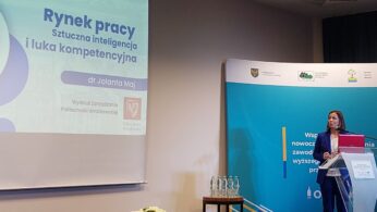 Kobieta stoi na podium i mówi do mikrofonu podczas prezentacji. Slajd na ekranie głosi: 