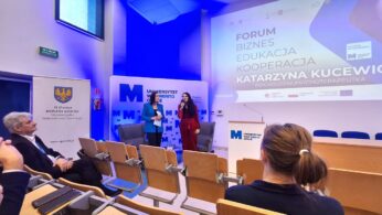 Dwie kobiety stoją na scenie z mikrofonami przed dużym ekranem na Uniwersytecie Opolskim. Na ekranie wyświetlany jest napis 