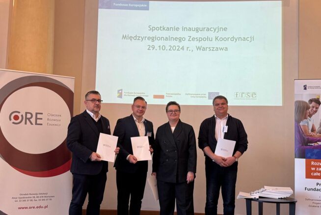 Cztery osoby stoją obok siebie w strojach biznesowych, trzy trzymają certyfikaty. Za nimi ekran projekcyjny wyświetla polski tekst o inauguracyjnym spotkaniu międzyregionalnego zespołu koordynacyjnego w dniu 29.10.2024 r. w Warszawie. Po obu stronach widoczne są dwa zwijane banery.