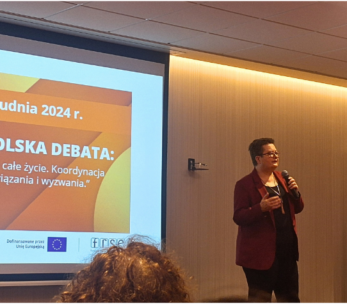 Prelegent stoi z mikrofonem przed ekranem wyświetlającym slajd dotyczący krajowej debaty na temat uczenia się przez całe życie w Polsce w dniach 16-17 grudnia 2024 roku. W sali znajdują się siedzący uczestnicy i baner Fundacji Rozwoju Systemu Edukacji.