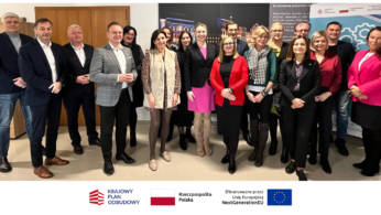 Grupa 16 profesjonalnie ubranych osób stoi w pomieszczeniu, uśmiechając się do kamery. Za nimi znajdują się plakaty z tekstem i obrazami. Pod zdjęciem widnieją trzy logotypy i nazwy - Krajowy Plan Odbudowy, Rzeczpospolita Polska i Unia Europejska.