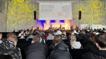 Duża publiczność siedzi w rzędach naprzeciwko sceny na 
