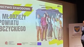 Kobieta stoi na podium i przemawia, a obok niej na dużym ekranie widać grupę wiwatujących młodych ludzi i polski tekst: Dla młodzieży powiatu głubczyckiego. Na ekranie i podium wyświetlane są oficjalne logotypy i herb.