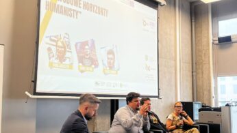 Cztery osoby siedzą na panelu dyskusyjnym w nowoczesnym pokoju. Jeden mężczyzna mówi do mikrofonu, podczas gdy inni słuchają. Za nimi duży ekran wyświetla wydarzenie Festiwal Kariery Zawodowe Horyzonty Humanistyki wraz z nazwiskami i zdjęciami panelistów.