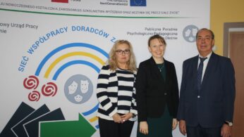 Trzy dorosłe osoby, dwie kobiety i jeden mężczyzna, stoją uśmiechnięte w strojach biznesowych przed wyświetlaczem z polskim tekstem, symbolami i logo programów edukacyjnych i unijnych. Tło zawiera niebieskie strzałki, obrazy sieci i oficjalne logo.
