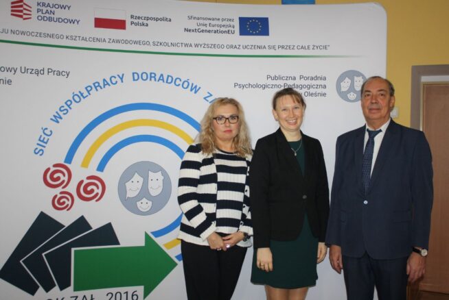 Trzy dorosłe osoby, dwie kobiety i jeden mężczyzna, stoją uśmiechnięte w strojach biznesowych przed wyświetlaczem z polskim tekstem, symbolami i logo programów edukacyjnych i unijnych. Tło zawiera niebieskie strzałki, obrazy sieci i oficjalne logo.