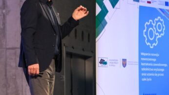 Mężczyzna w okularach, ciemnej marynarce i szarych spodniach przemawia na scenie obok niebiesko-białego banera promocyjnego. Baner wyświetla polski tekst o rozwoju edukacji i logo organizacji wspierających. Tło stanowi przemysłowa, betonowa ściana.