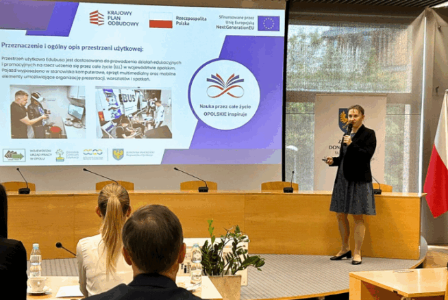 Kobieta w ciemnej sukience prezentuje pokaz slajdów w sali konferencyjnej. Slajd zawiera polski tekst, logo, zdjęcia pracujących ludzi i wspomina o Unii Europejskiej. Siedzący uczestnicy są zwróceni w jej stronę, a po prawej stronie wyświetlane są flagi Polski i UE.