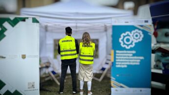 Dwie osoby w jaskrawożółtych kamizelkach ochronnych z napisem 