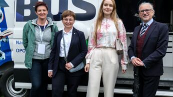 Cztery dorosłe osoby - trzy kobiety i jeden mężczyzna - stoją uśmiechnięte przed furgonetką z dużym napisem 