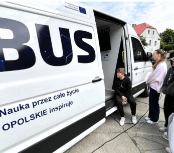 Grupa młodych ludzi stoi przed białą furgonetką z dużym napisem "BUS". Jedna osoba przykuca przy otwartych bocznych drzwiach. Na furgonetce widnieje polski tekst: "Nauka przez cale zycie OPOLSKIE inspiruje". W tle widoczne są budynki i drzewa.