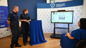 Dwóch policjantów stoi przy ekranie wyświetlającym wykres, prezentując siedzącą kobietę w niebieskiej sukience. Sceneria wydaje się być klasą lub seminarium z niebieskim podium, banerami i wyświetlaczem z napisem 