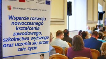 Baner informacyjny z napisem „wsparcie rozwoju kształcenia zawodowego i uczenia się przez całe życie. W tle uczestnicy siedzący tyłem na sali konferencyjnej.”