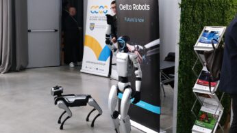 Dwa roboty, jeden humanoidalny i jeden czworonożny, stoją obok baneru 