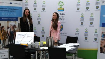Dwie kobiety stojące na stoisku promocyjnym z logo Opolskiego Centrum Edukacji.