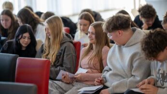 Uczestnicy rozwiązują zadania, związane z doradztwem zawodowym. Siedzą na kolorowych krzesłach w rzędach na sali wykładowej.