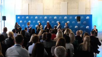 Uczestnicy konferencji siedzą na widowni, obserwując panel dyskusyjny. Na scenie siedzi sześć osób.