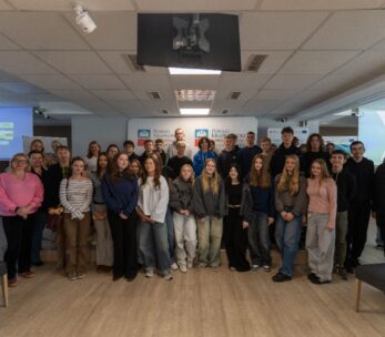 Duża grupa młodych ludzi i kilku dorosłych pozuje do wspólnego zdjęcia w sali konferencyjnej, w tle logo Powiatu Krapkowickiego.