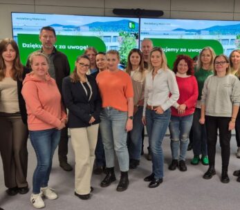 Grupowe zdjęcie kilkunastu uczestników (mężczyzn i kobiet) w sali konferencyjnej. Stoją oni przed ekranami, na których wyświetlone są zielone slajdy z logo Heidelberg Materials i napisem "Dziękujemy za uwagę!".