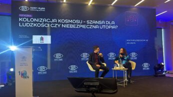 Zdjęcie z panelu dyskusyjnego na dużej scenie z ogromnym ekranem w tle, podczas konferencji 