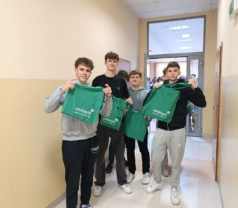 Czterech młodych mężczyzn stoi w korytarzu, uśmiechając się do aparatu i trzymając zielone torby z logo firmy Umicore. W tle widać otwarte drzwi do pomieszczenia. Na podłodze widoczny jest napis "CKP NYSA", sugerujący lokalizację wydarzenia.