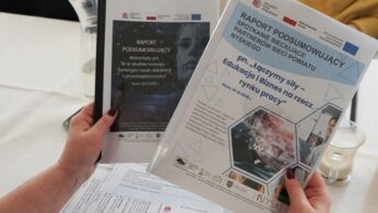 Widok na dłonie uczestniczki spotkania, która trzyma w dłoni „Raport podsumowujący spotkanie sieciujące ” oraz „Raport podsumowujący warsztaty…”. Dokumenty zawierają ciągi znaków projektu Krajowego Planu Odbudowy i Zwiększania Odporności oraz Współrealizatorów projektu „Wsparcie rozwoju nowoczesnego kształcenia zawodowego, szkolnictwa wyższego oraz uczenia się przez cale życie”.