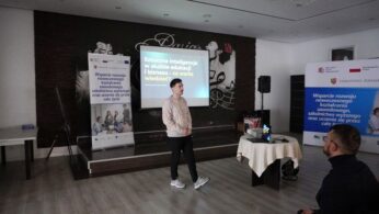 Ujęcie przedstawiające prelegenta na scenie, prezentującego slajd z tytułem 