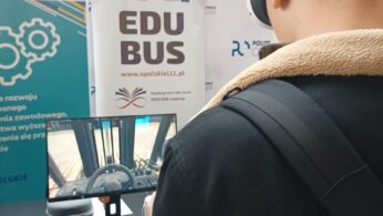 Ujęcie od tyłu, młodego ucznia z założonymi goglami VR. Uczeń skierowany jest w stronę ekranu, na którym wyświetla się kadr z aplikacji „Widzę siebie w tym zawodzie”. W tle, za ekranem znajduje się banner promujący projekt 