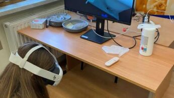 Zdjęcie z bliska przedstawia uczennicę z długimi włosami siedzącą na podłodze i używającą gogli wirtualnej rzeczywistości oraz kontrolerów. Na ekranie monitora widoczna jest symulacja zabiegu kosmetycznego, prawdopodobnie wstrzykiwania botoksu, co nawiązuje do tekstu o szkoleniu. Scena pokazuje praktyczne i nowoczesne podejście EduBusa do nauki zawodów.