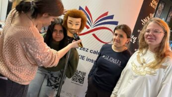 Grupa czterech młodych kobiet pozuje przy białym banerze z napisem „Nauka przez całe życie”. Jedna z nich trzyma maszynkę fryzjerską przy głowie treningowej zamontowanej na statywie, imitując strzyżenie. Na podłodze leżą ścięte kosmyki włosów, a w tle widoczne jest logo „Barber Shop”.