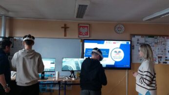 Uczniowie testują sprzęt VR pod okiem nauczycielki w sali szkolnej wyposażonej w monitory i interaktywny ekran. Na głównym wyświetlaczu widnieje logo projektu „Opolskie Inspiruje” oraz informacje o nauce przez całe życie. Wnętrze jest jasne, z szafkami i gazetkami ściennymi w tle. Na ścianie wisi zegar wskazujący godzinę 10:08.
