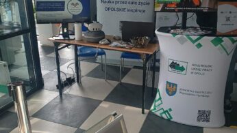 Stanowisko Wojewódzkiego Urzędu Pracy w Opolu z banerem pod hasłem „Nauka przez całe życie – OPOLSKIE inspiruje”. Na biurku przygotowano zestaw VR do wirtualnego poznawania zawodów, a na monitorach wyświetlane są materiały informacyjne. Obok stoi biały stand z logo urzędu oraz kodem QR.