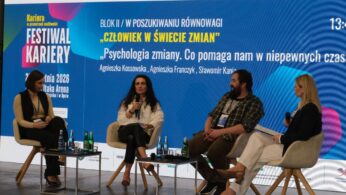 Ujęcie stoiska informacyjnego, przy którym przedstawicielka instytucji rozmawia z zainteresowanym uczestnikiem. Na blacie rozłożone są materiały edukacyjne, broszury oraz gadżety promocyjne. W tle widoczne są ścianki wystawiennicze z logotypami organizatorów.