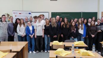 Pamiątkowe, grupowe zdjęcie uczniów i nauczycieli w sali lekcyjnej, stojących przed zieloną tablicą z napisem 