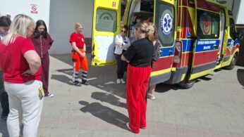 Ratownicy medyczni przy karetce pogotowia podczas wizyty edukacyjnej lub szkolenia przed budynkiem