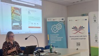 Prelegentka prezentująca slajdy podczas spotkania, widoczne banery informacyjne i ekran projekcyjny