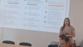 Prelegentka omawia prezentację przed uczestnikami spotkania, na ekranie widoczne są materiały informacyjne.
