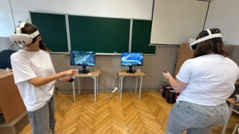 Dwie osoby podczas zajęć z wykorzystaniem gogli VR wykonują ćwiczenia przy stanowiskach komputerowych.