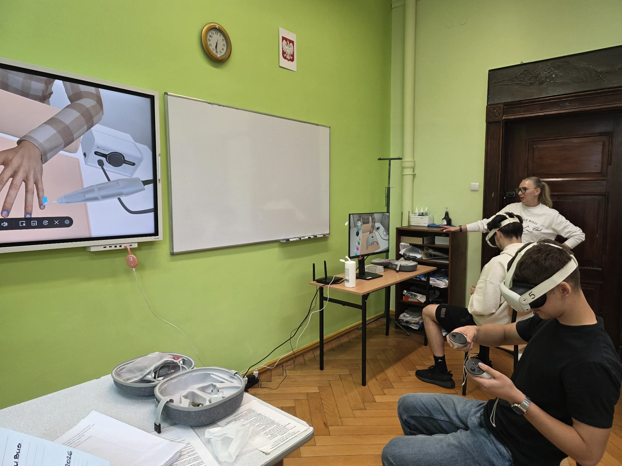 Sala lekcyjna z wyposażeniem do zajęć VR, uczestnik korzysta z gogli wirtualnej rzeczywistości przy stanowisku komputerowym.