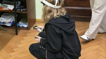 Osoba siedząca na podłodze korzysta z gogli VR podczas praktycznych zajęć edukacyjnych.