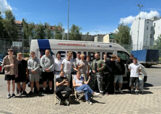 Grupa uczestników stoi przed autobusem podczas wyjazdu lub wydarzenia edukacyjnego.