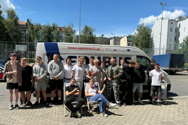 Grupa uczestników stoi przed autobusem podczas wyjazdu lub wydarzenia edukacyjnego.