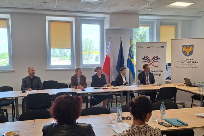 Spotkanie w sali konferencyjnej z udziałem prelegentów i uczestników, prezentacja materiałów na ekranie oraz rozmowy przy stole.