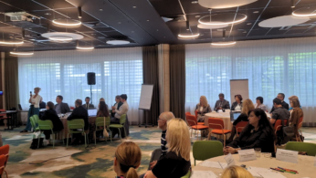 Uczestnicy spotkania siedzą przy stołach w sali konferencyjnej podczas warsztatów lub dyskusji grupowej.